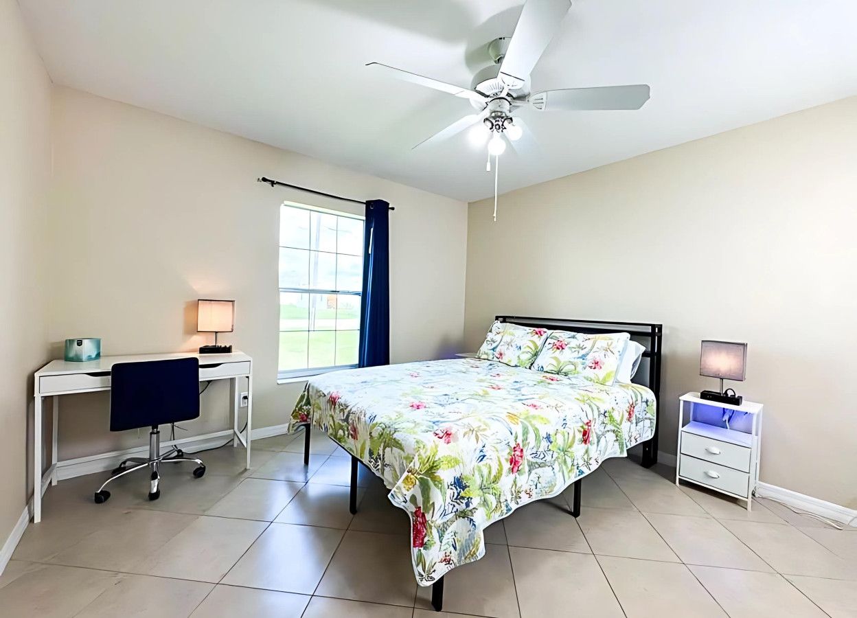 Ein Schlafzimmer mit einem Bett, einem Schreibtisch, einem Stuhl, einem Nachttisch und einem Deckenventilator.