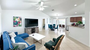 A spacious living room with a flat-screen TV, blue sofa, and a dining area with chairs and a table. - 3BR Waterfront Views | Pool + BBQ | 3 King Beds | Sleeps 7 | Port Charlotte (Port Charlotte)