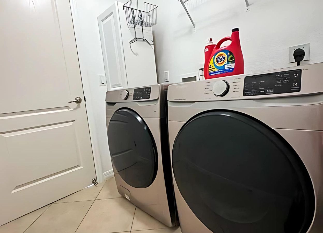 Un lavadero con dos lavadoras de carga frontal y una botella de detergente Tide encima.