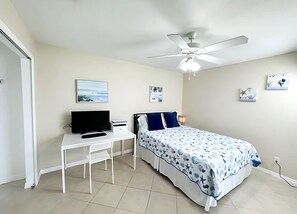 Ein Schlafzimmer mit einem Bett, einem Schreibtisch, einem Sessel, einem Deckenventilator und Kunstwerken an den Wänden.