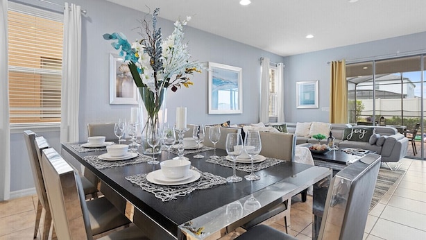 A dining area with a black table set for six, surrounded by chairs, in a room with a grey wall and a large window. - 7BR Star Wars Room | Pool+HotTub | Windsor Resort | Disney 10 Min | Sleeps 16 (Kissimmee)