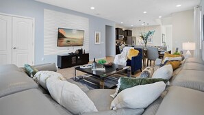 A modern living room with a sofa, coffee table, TV, and a dining area with chairs and a table. - 7BR Star Wars Room | Pool+HotTub | Windsor Resort | Disney 10 Min | Sleeps 16 (Kissimmee)