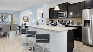 A modern kitchen with dark cabinets, stainless steel appliances, and a central island with bar stools. - 7BR Star Wars Room | Pool+HotTub | Windsor Resort | Disney 10 Min | Sleeps 16 (Kissimmee)
