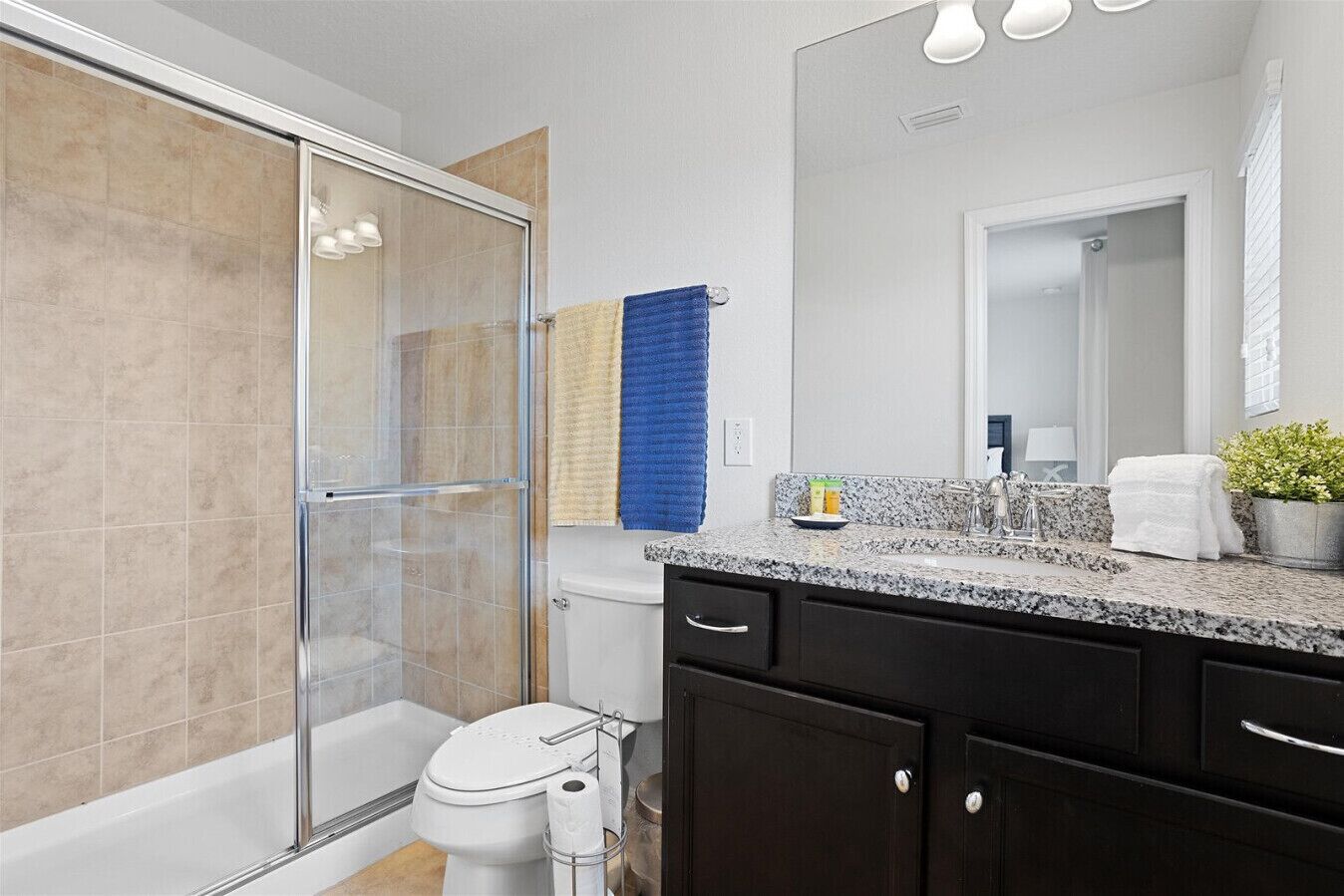 A modern bathroom with a glass shower enclosure, a toilet, a sink with a granite countertop, and dark cabinetry.