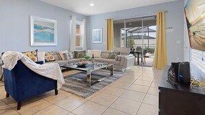 A living room with a sofa, coffee table, and a TV. There is a glass door leading to an outdoor area. - 7BR Star Wars Room | Pool+HotTub | Windsor Resort | Disney 10 Min | Sleeps 16 (Kissimmee)
