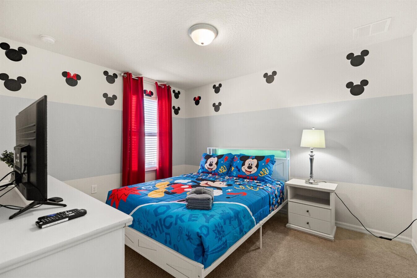 A bedroom with a bed, a desk, a TV, and a lamp.