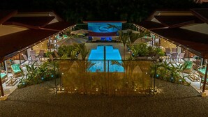 Zona de piscina con una gran pantalla que muestra un delfín, rodeada de sillas de descanso y plantas en macetas.