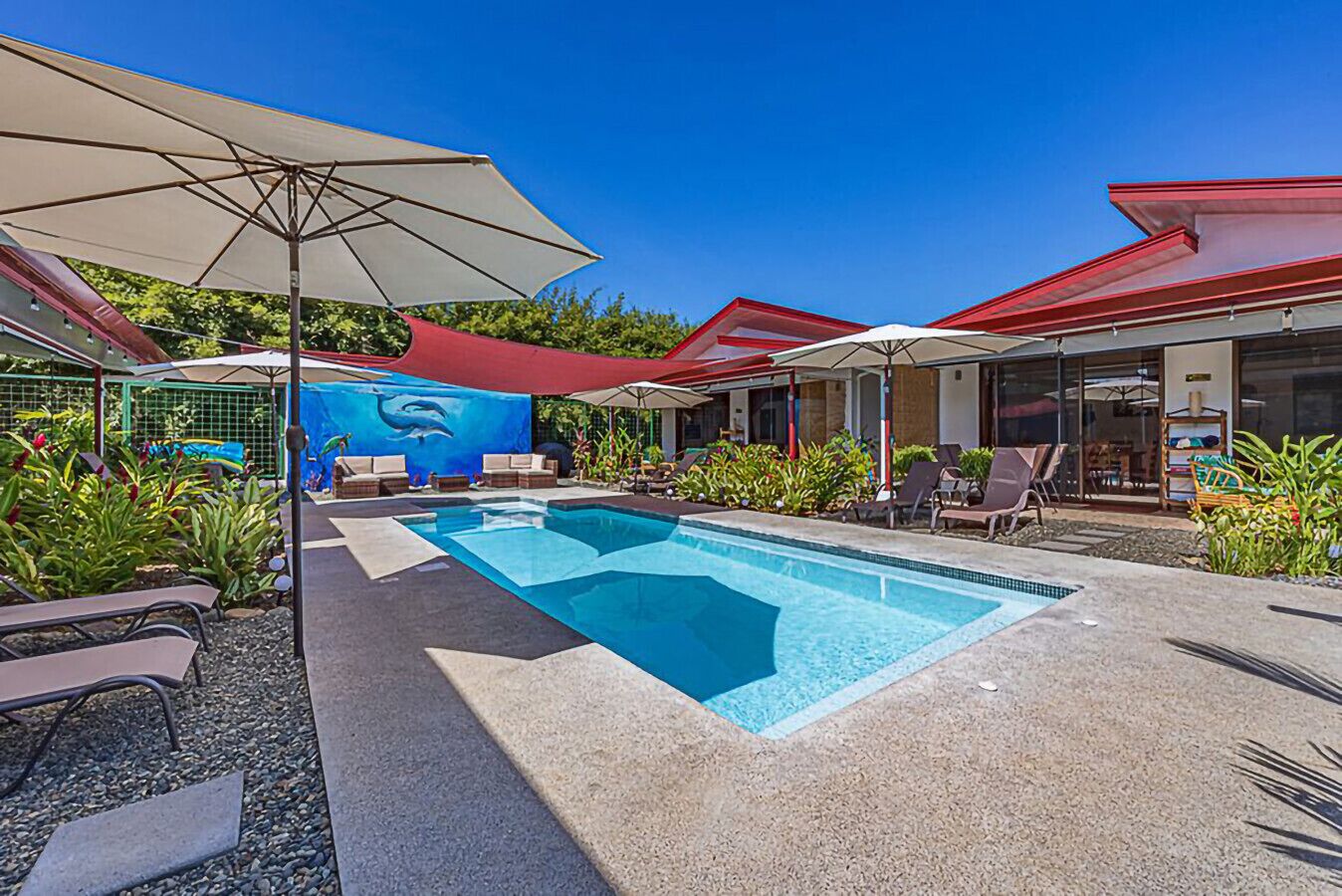 A swimming pool with lounge chairs and umbrellas, surrounded by greenery and a mural.