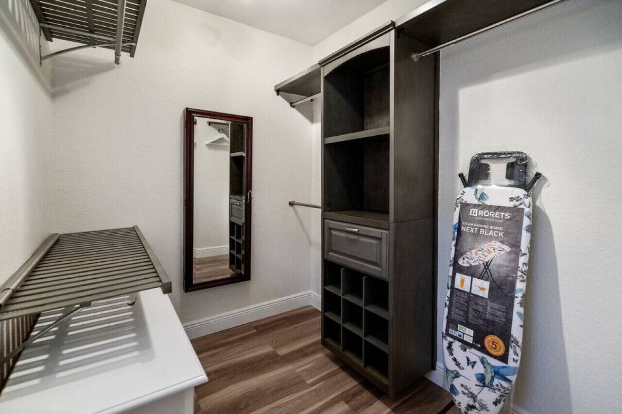 A compact room with a built-in wardrobe, a mirror, and a steam ironing board.