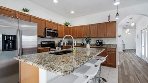 Eine moderne Küche mit Granit-Arbeitsplatten, Edelstahlgeräten, Holzschränken und einer Bar mit Hockern.