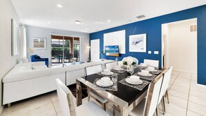 Un espace repas moderne avec une table noire dressée pour quatre personnes, des chaises blanches et un canapé blanc en arrière-plan.