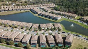Une vue aérienne d’un quartier résidentiel où de nombreuses maisons sont disposées en rangées, avec un plan d’eau central et une fontaine.