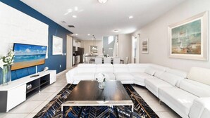 Un salon moderne avec un canapé d’angle blanc, une table basse foncée et un téléviseur à écran plat.