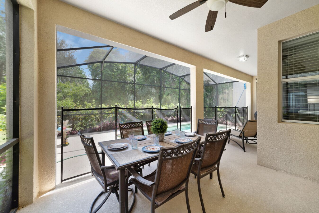 A covered patio with a table set for dining, surrounded by chairs, and a ceiling fan above.
