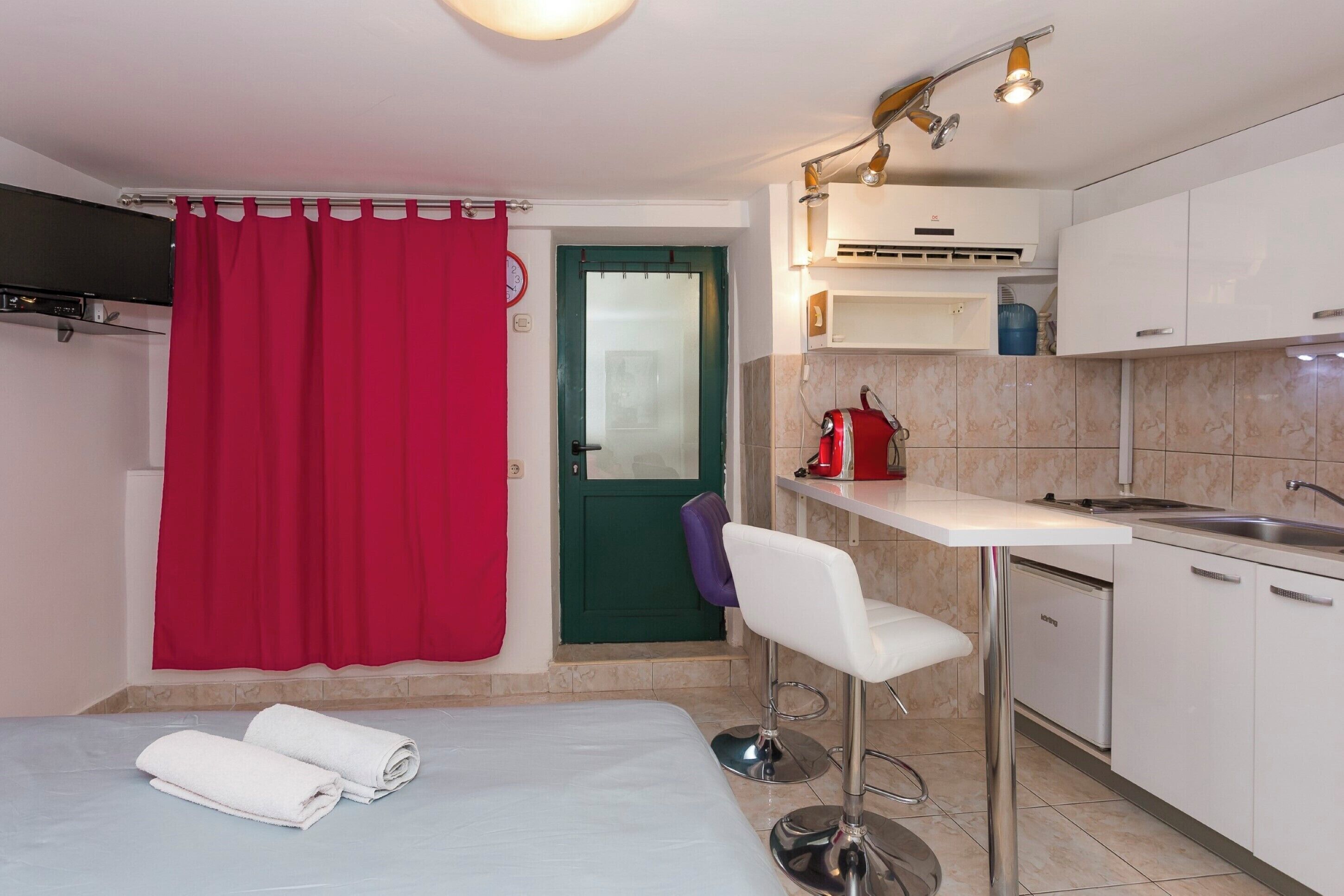 A compact kitchen with a white countertop, a sink, and a red curtain.