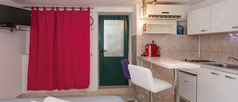 A compact kitchen with a white countertop, a sink, and a red curtain.