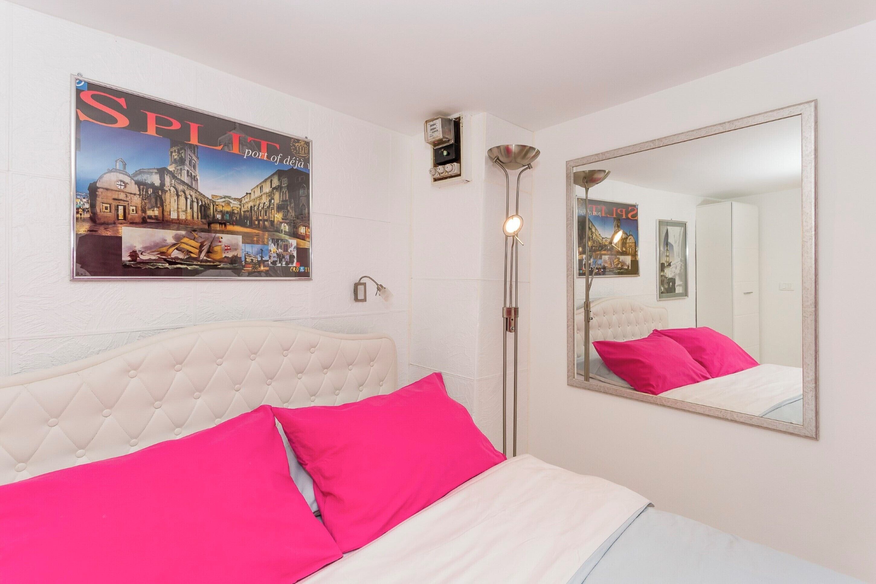 Une chambre d’hôtel avec un lit, un grand miroir et une affiche représentant un paysage urbain.
