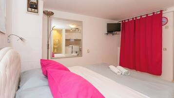 Habitación de hotel con una cama, un espejo, un televisor y una cortina roja.