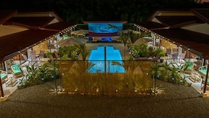 A pool area with a large screen displaying a dolphin, surrounded by lounge chairs and potted plants. - Villa Colibri, Uvita, 1BR/1BA poolside, near beach (Uvita)