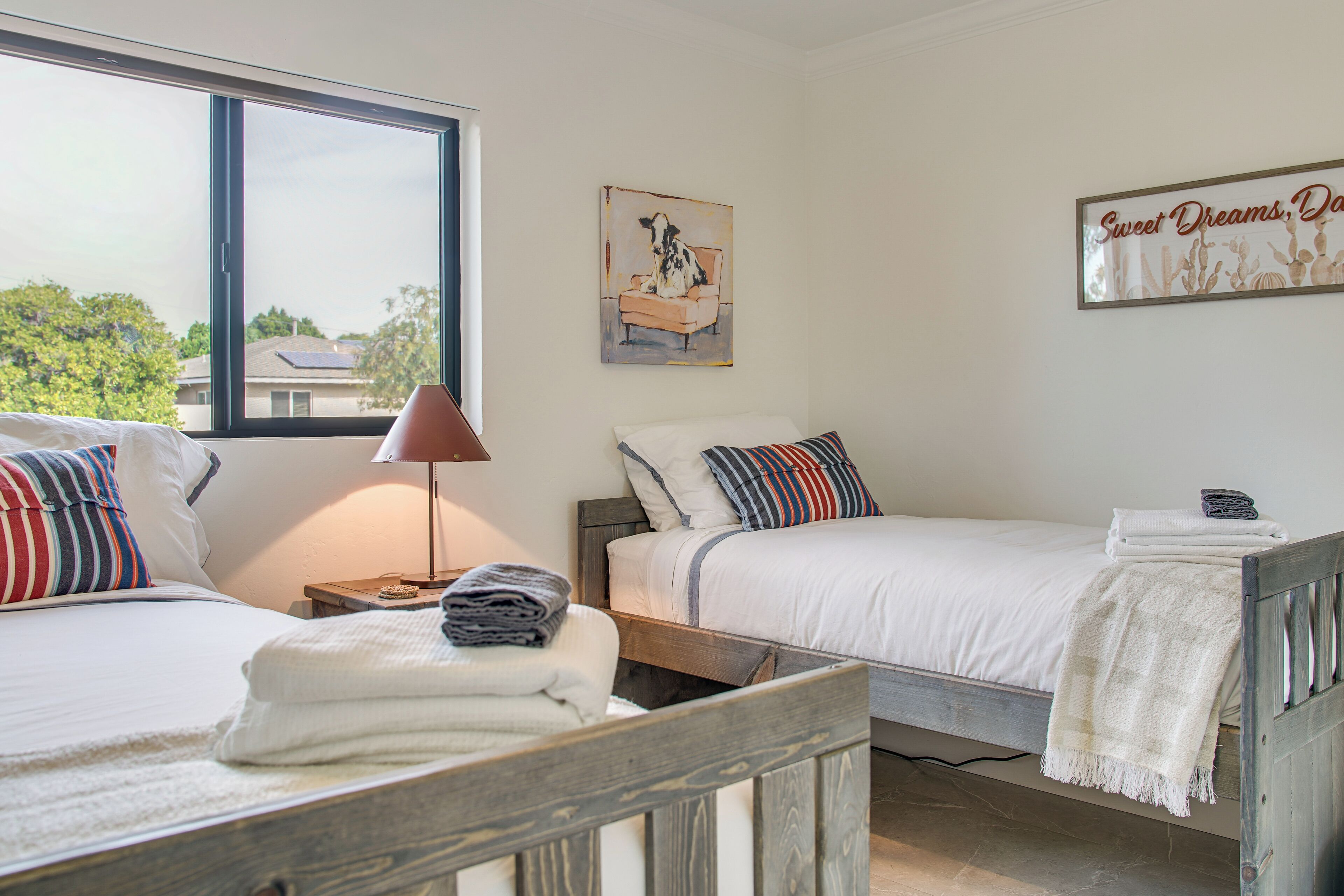 A bedroom with two beds, a window, and a painting on the wall.