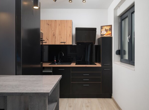 A compact kitchen with dark cabinetry, a wooden countertop, and a black refrigerator.