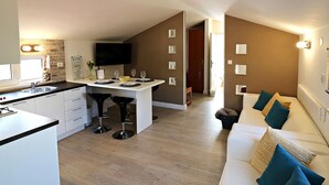Una cocina moderna con comedor, un televisor de pantalla plana y una sala de estar acogedora con sofá y cojines.