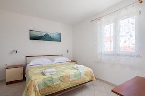 Ein Schlafzimmer mit einem Bett, einem Nachttisch, einem Holztisch, einem Fenster mit Vorhängen und einem Bild an der Wand.