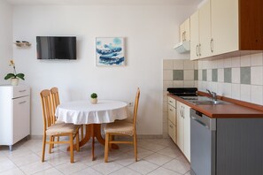 Eine kompakte Küche mit Essbereich, einem an der Wand montierten Fernseher und einem kleinen Blumentopf auf dem Tisch.