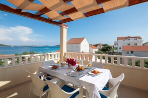 Una terraza con mesa lista para el desayuno, con vista al mar y casas a la orilla.
