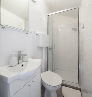 Un baño moderno con cabina de ducha de vidrio, un lavabo blanco con repisa de cristal y un inodoro.
