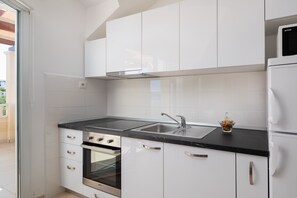Ett modernt kök med vita skåp, en svart bänkskiva, rostfria vitvaror och en glasdörr som leder ut till ett utomhusområde.