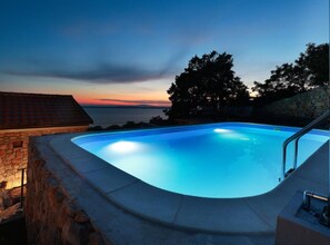 Ein Swimmingpool mit einer Steinmauer und Blick auf den Sonnenuntergang.