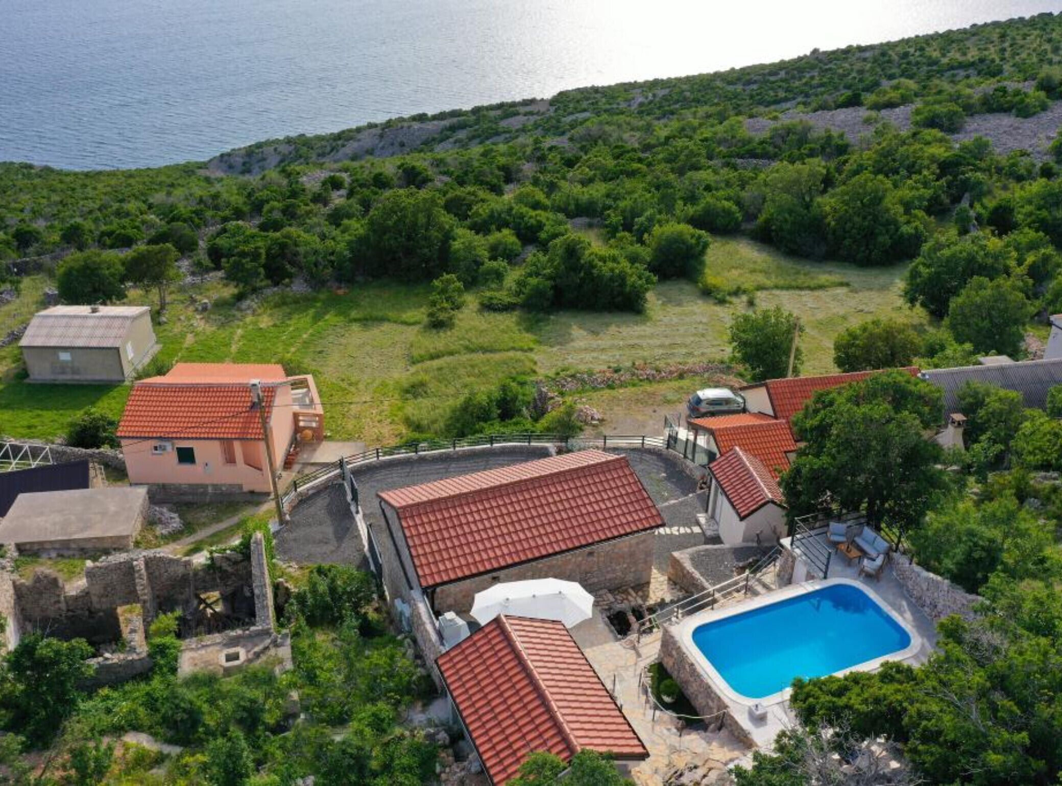 A coastal property with a swimming pool, red-tiled roofs, and a view of the sea.