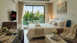 A hotel room with a bed, a TV, a dining table with chairs, and a balcony with plants. - Laguna beach resort maldives 3 - Modern studio pool view with balcony in Jomtien (Muang Pattaya)