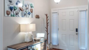 A hallway with a wooden console table, a lamp, a vase, and a door with blinds. - Perfect Stop • Near I-95, Downtown & Civic Center and Darlington (Florence)