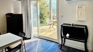 A room with a sliding glass door leading to an outdoor patio, a small table, a chair, and a black cabinet.