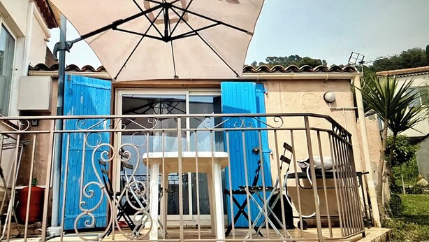 A balcony with a metal railing, a beige umbrella, and blue shutters.
