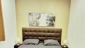 A modern bedroom with a wooden bed frame, a dark-colored bedspread, and a headboard with a picture.