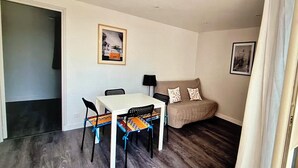 A compact living space with a dining table and chairs, a sofa, and two framed pictures on the walls.