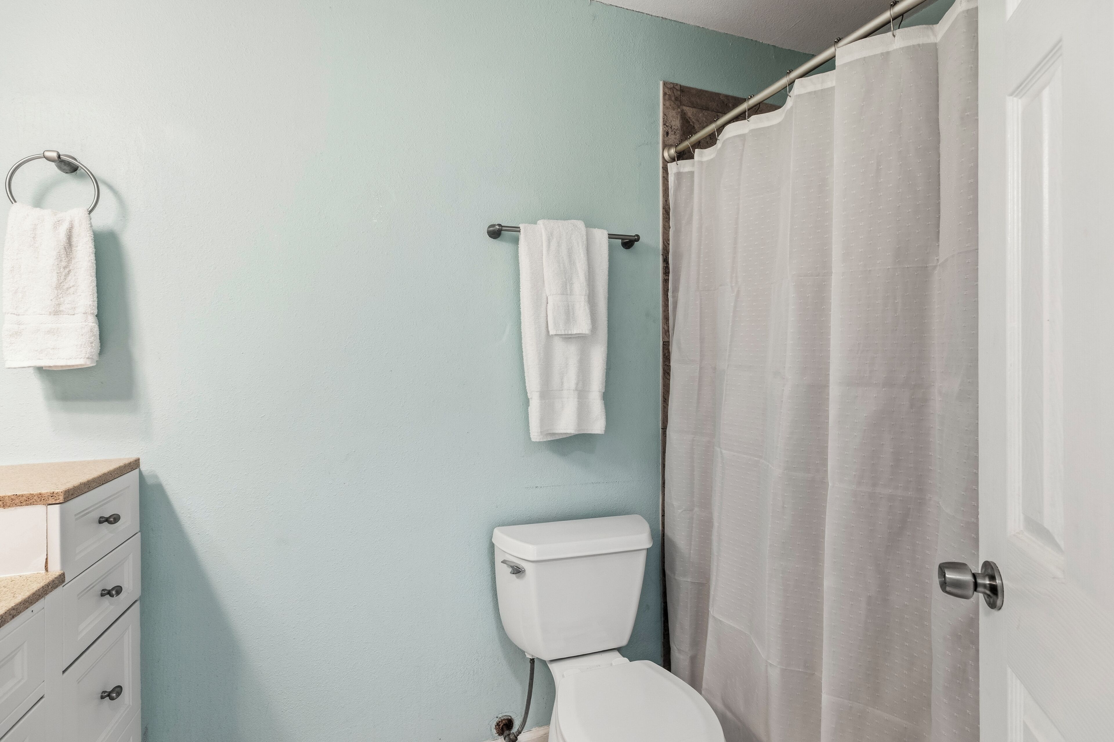 A bathroom with a toilet, a towel rack, a shower curtain, and a wooden cabinet.