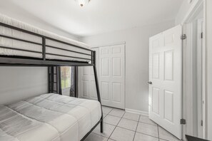 Habitación con literas, puerta blanca y suelo de baldosas.