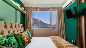 Ein Hotelzimmer mit Bett, Fernseher und Fenster mit Blick auf Berg und Stadtpanorama.