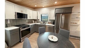 Een moderne keuken met witte kastjes, roestvrijstalen apparatuur en een ronde eettafel met grijze stoelen.