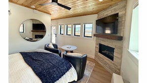 Een slaapkamer met een bed, een ronde spiegel, een open haard en een plafondventilator.