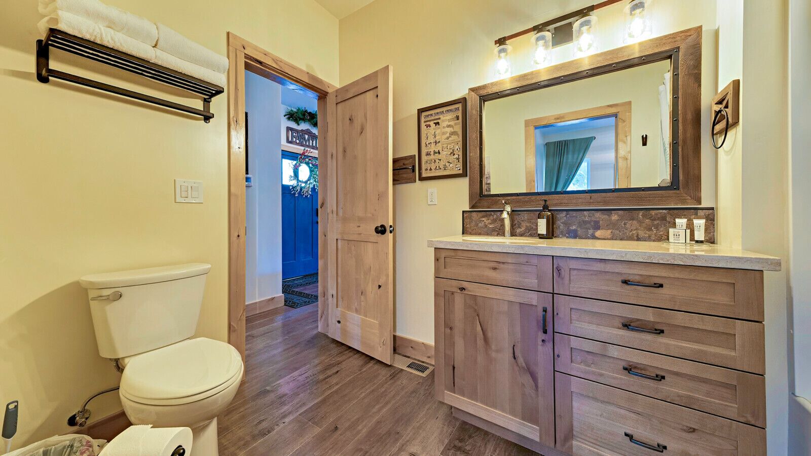 A bathroom with a toilet, wooden vanity with drawers, a mirror, and a towel rack.