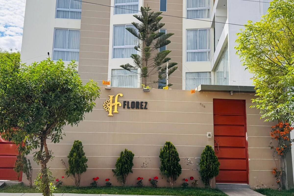 Un hotel de varios pisos con fachada color beige, una puerta de entrada roja y un letrero que dice "FLOREZ".