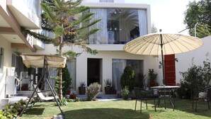 A modern house with a patio area featuring a swing chair, a table with chairs, and a large umbrella. - hotel florez boutique (Arequipa)