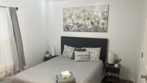 A bedroom with a bed, a headboard, a nightstand, a bedside table, a window with curtains, and a wall-mounted painting. - 3 Bedroom 3 Bath Townhome Cul-de-Sac (Tallahassee)