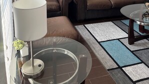 A living room with a brown leather sofa, a glass coffee table, and a painting of vases on the wall. - 3 Bedroom 3 Bath Townhome Cul-de-Sac (Tallahassee)
