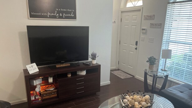 A living room with a flat-screen TV, dark wood entertainment center, glass coffee table, and a cozy sofa. - 3 Bedroom 3 Bath Townhome Cul-de-Sac (Tallahassee)